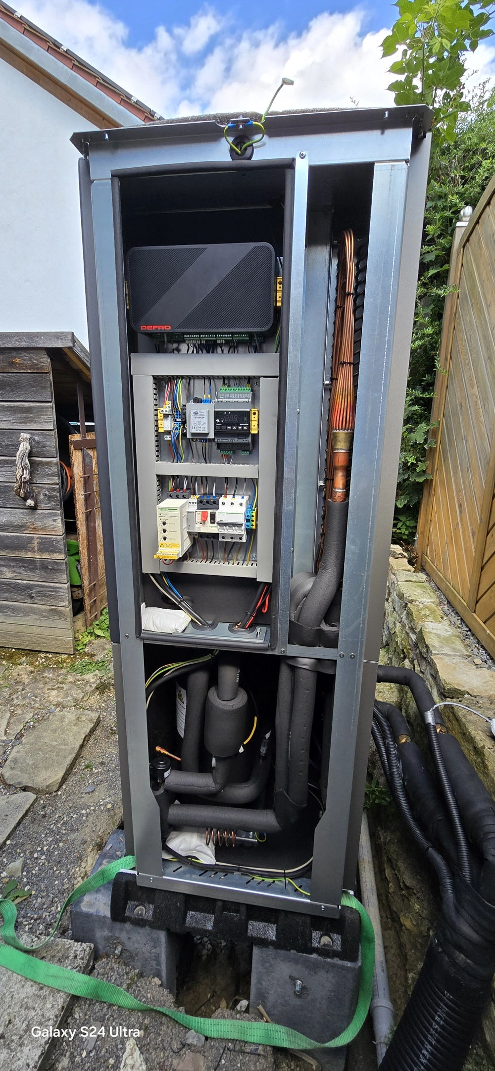 Montaż pompy ciepła z otwartą obudową, widocznymi modułami elektronicznymi, przewodami i izolowanymi rurami