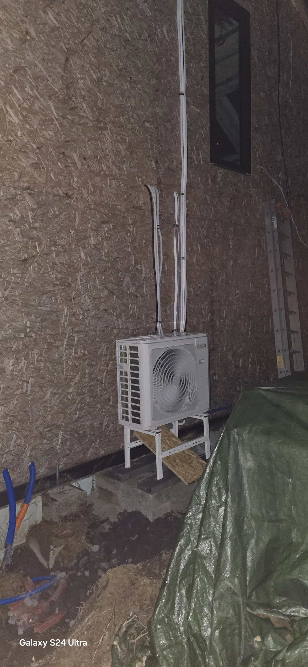 Montaż pompy ciepła powietrze woda – zewnętrzna jednostka na stelażu przy ścianie z trasami kablowymi