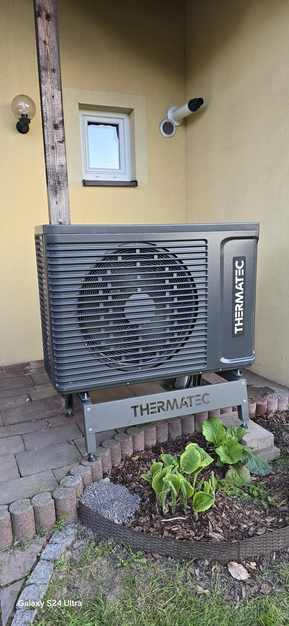 Zewnętrzna jednostka pompy ciepła powietrze-woda zamontowana przy elewacji na stalowej podstawie Montaż pompy ciepła