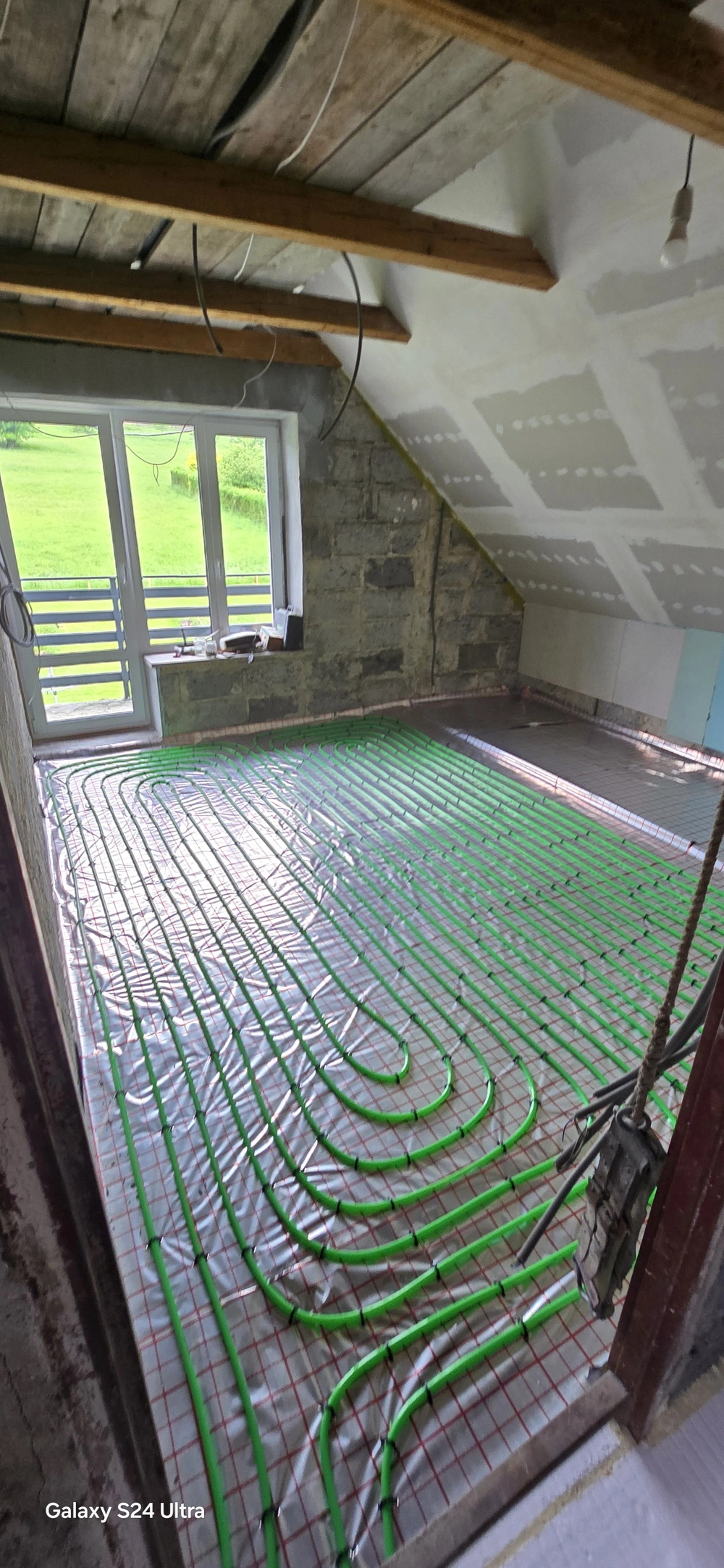 Pokój na poddaszu z widoczną instalacją ogrzewania podłogowego z zielonymi rurami