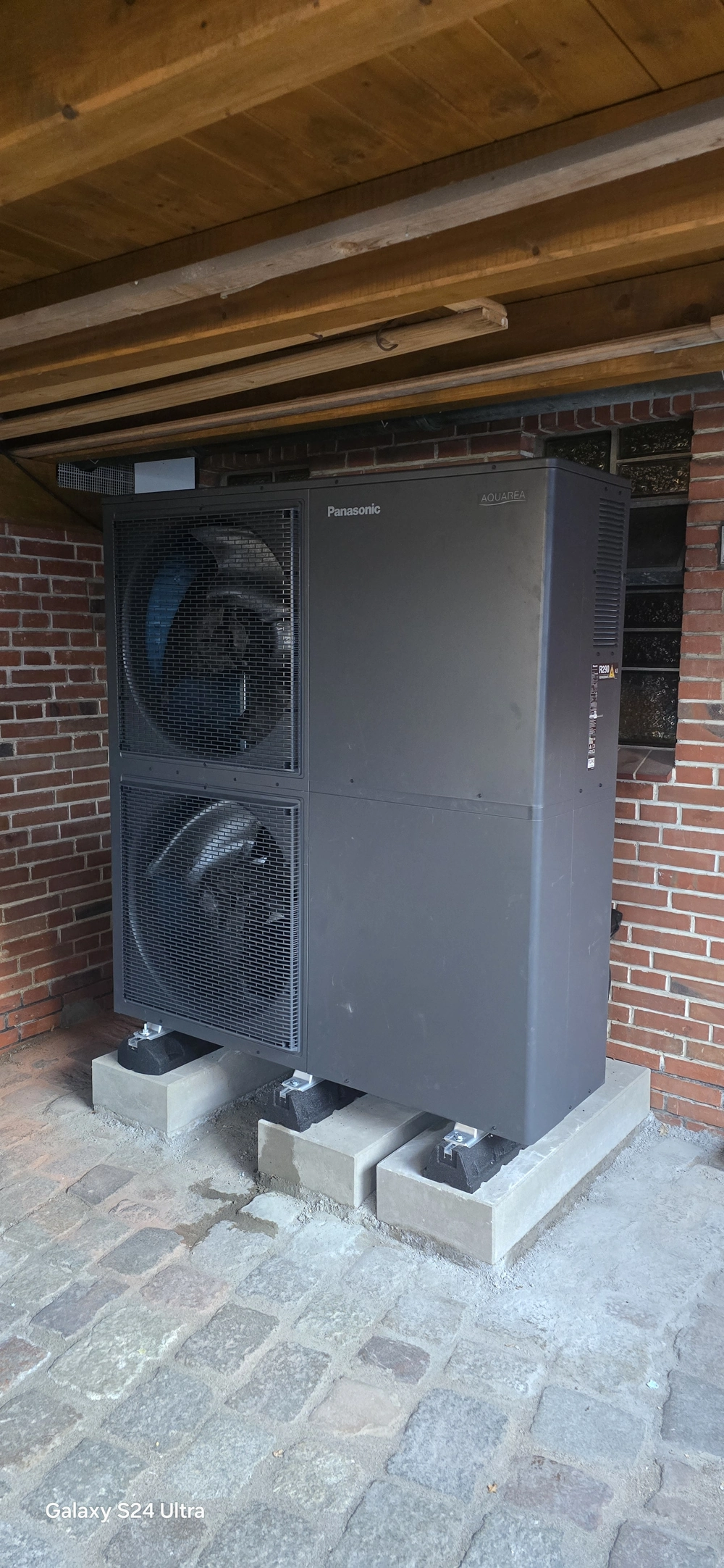 Jednostka pompy ciepła powietrze woda zamontowana na bloczkach przed ceglanym murem