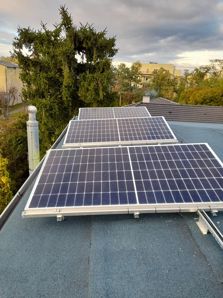 Panele fotowoltaiczne zamontowane na dachu płaskim budynku, widoczne uchwyty montażowe