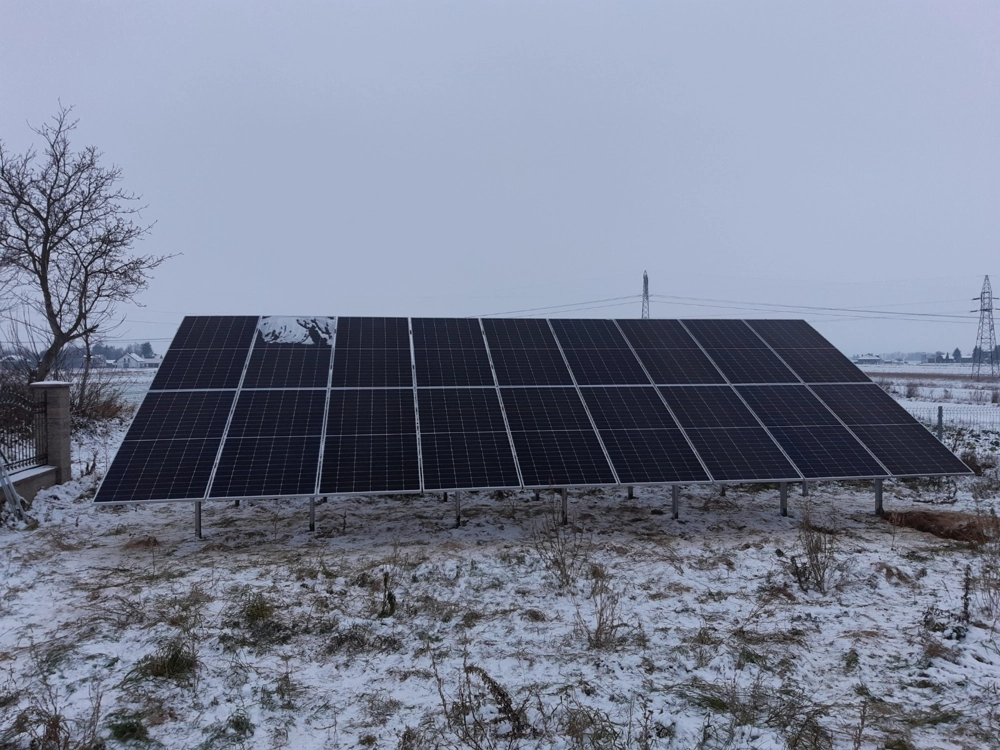 Panele fotowoltaiczne zamontowane na stelażu naziemnym na zaśnieżonym terenie