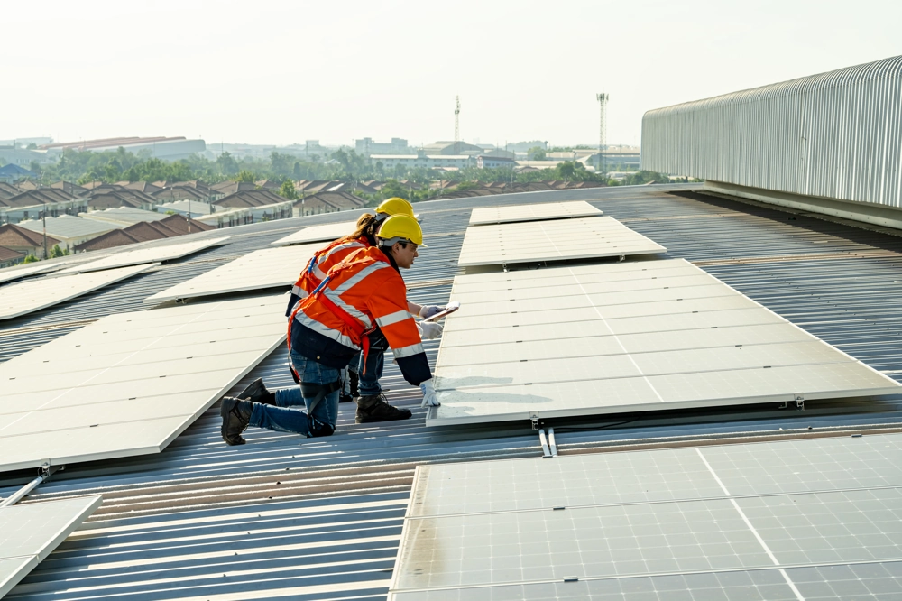 Dwóch monterów instaluje panele fotowoltaiczne na dachu budynku